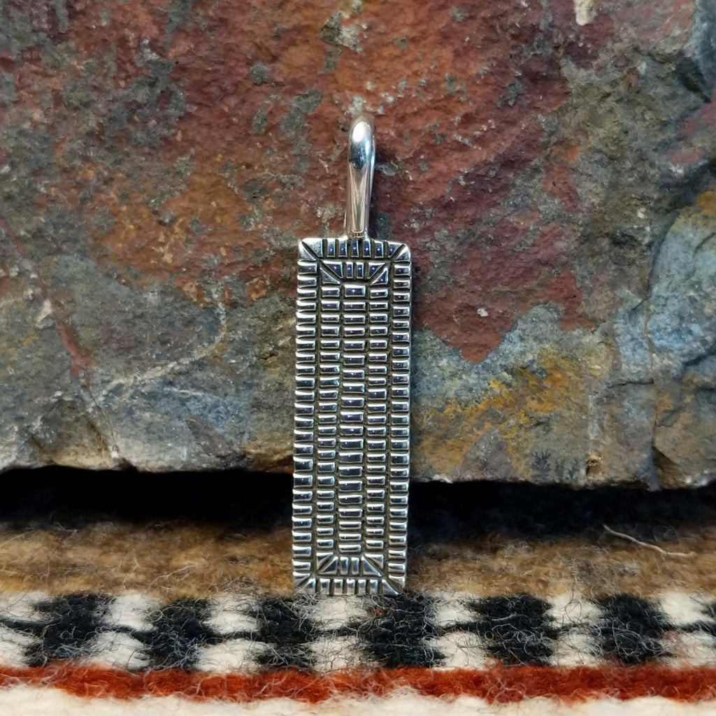 Rectangular sterling silver pendant with geometric stamping on the surface.