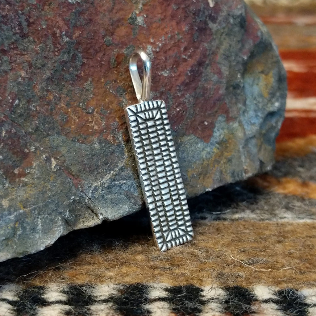 Rectangular sterling silver pendant with geometric stamping on the surface.