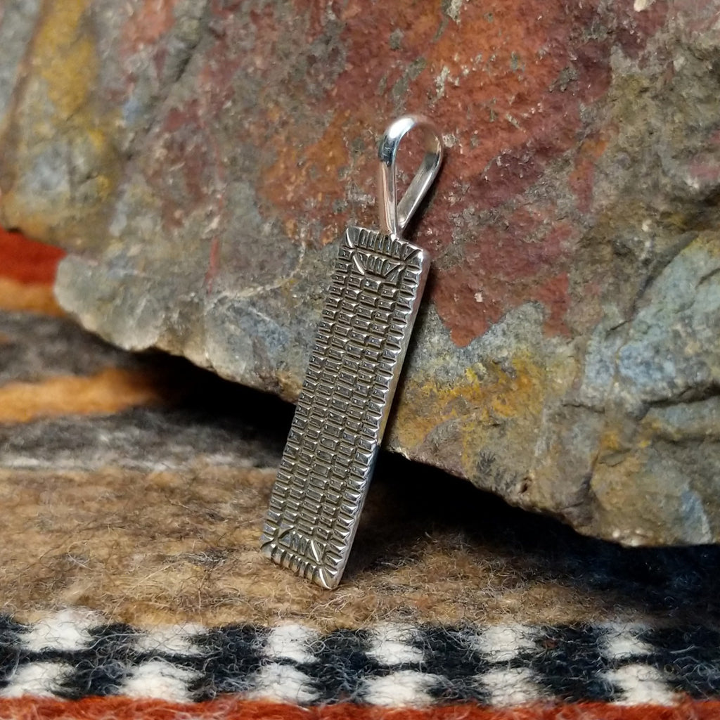 Rectangular sterling silver pendant with geometric stamping on the surface.