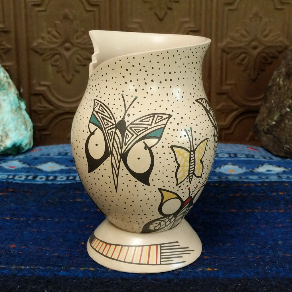 White clay body with black, red, and yellow butterfly designs and a stepped rim sat on a decorative display ring.
