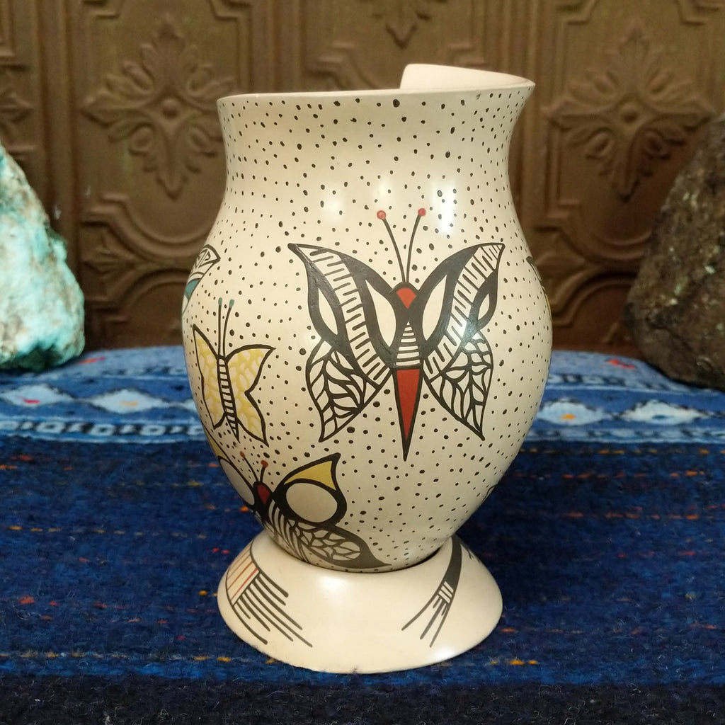 White clay body with black, red, and yellow butterfly designs and a stepped rim sat on a decorative display ring.