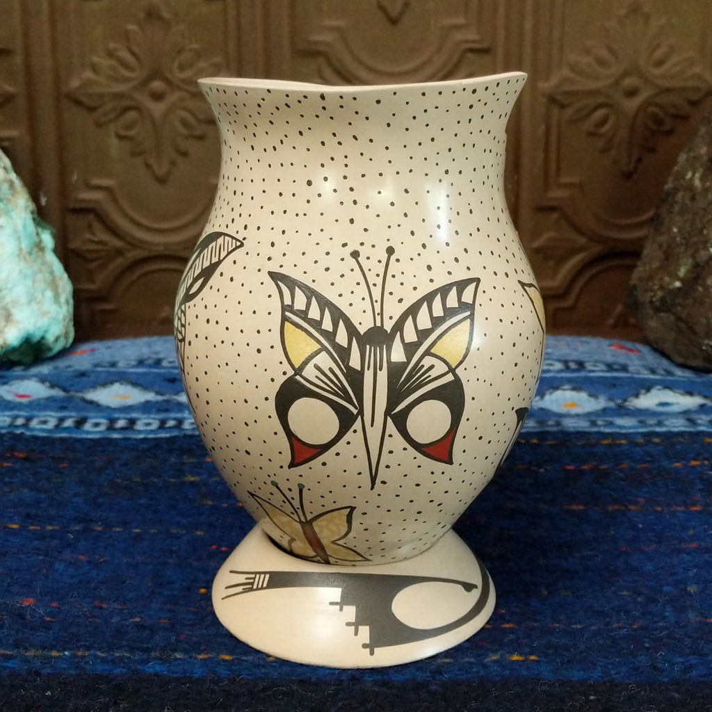 White clay body with black, red, and yellow butterfly designs and a stepped rim sat on a decorative display ring.