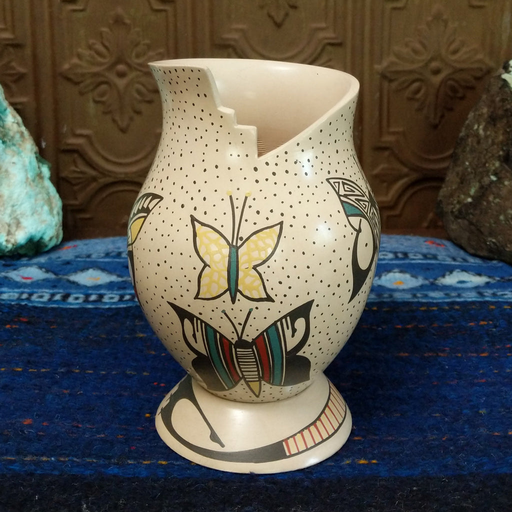 White clay body with black, red, and yellow butterfly designs and a stepped rim sat on a decorative display ring.