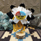 Navajo-made Sunface kachina doll by M. C. with circular multicolored mask, white feather halo, and yellow garments.
