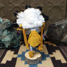 Navajo-made Sunface kachina doll by M. C. with circular multicolored mask, white feather halo, and yellow garments.