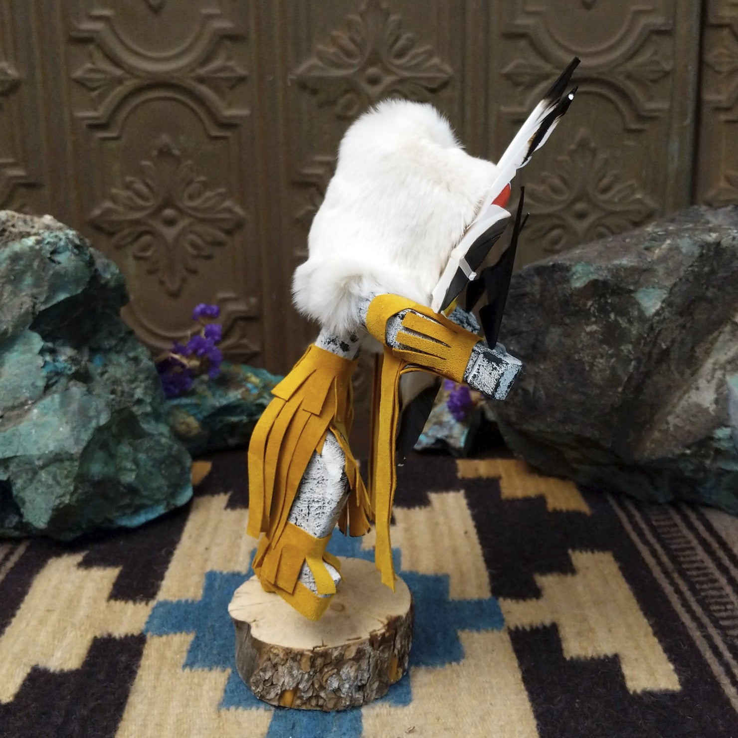 Navajo-made Sunface kachina doll by M. C. with circular multicolored mask, white feather halo, and yellow garments.