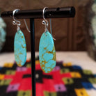 Tan Matrix Turquoise Slab Earrings by Ronald Chavez featuring elongated sky-blue turquoise stones with natural tan and golden-brown matrix, suspended from silver hooks; side view.