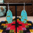 Tan Matrix Turquoise Slab Earrings by Ronald Chavez featuring elongated sky-blue turquoise stones with natural tan and golden-brown matrix, suspended from silver hooks; backside view.