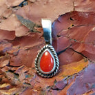 Teardrop-shaped pendant with coral, framed by twisted rope accent.