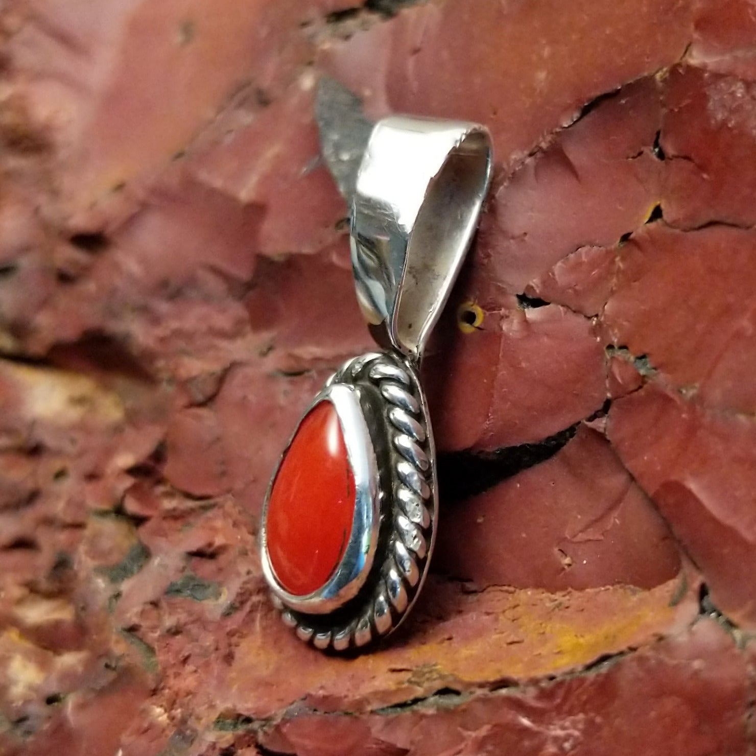 Teardrop-shaped pendant with coral, framed by twisted rope accent.