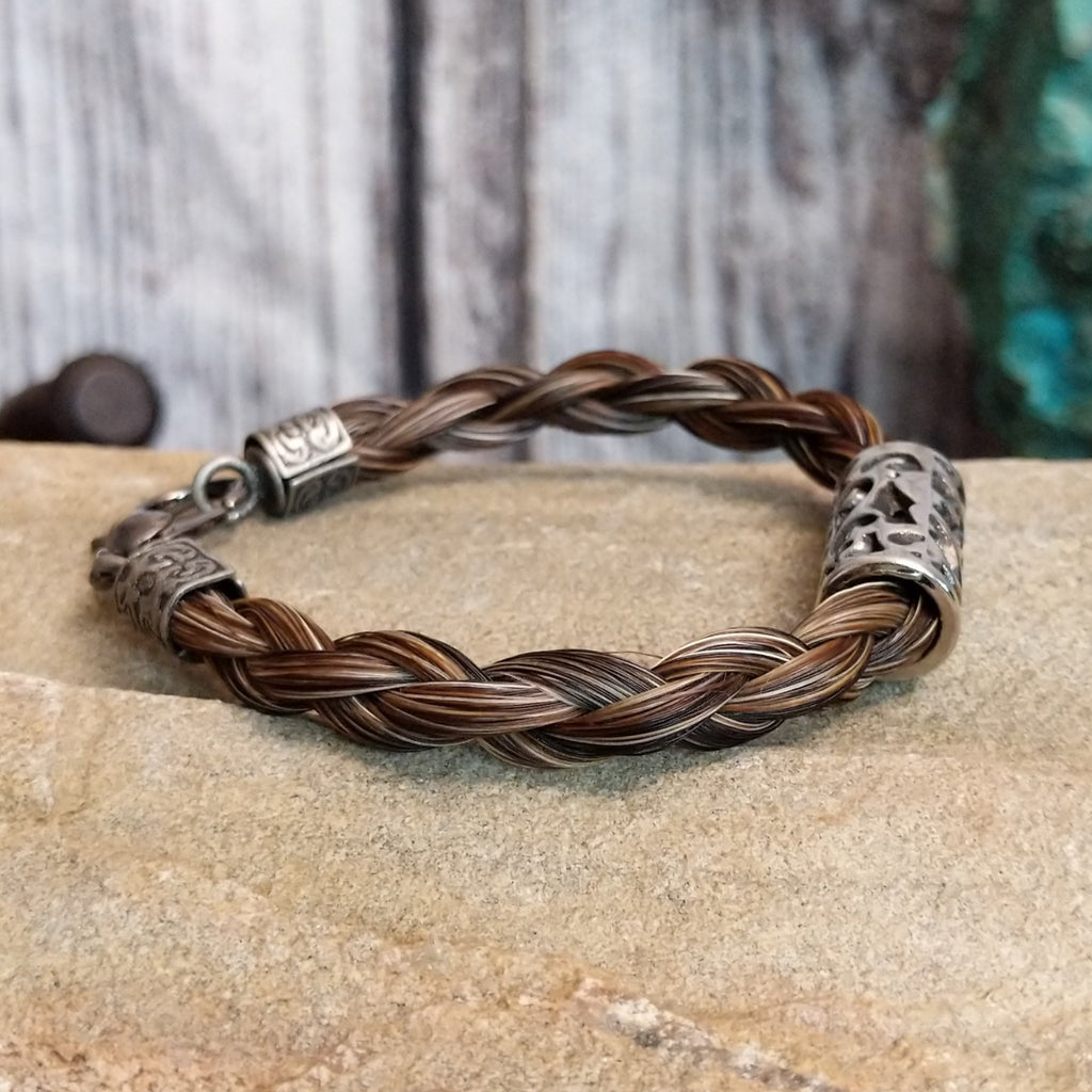 A braided multi-toned brown horsehair bracelet with an ornate metal design and metal clasp.