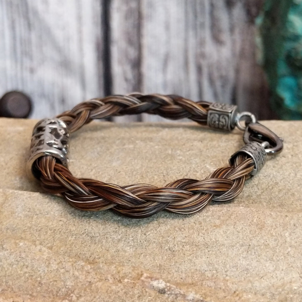 A braided multi-toned brown horsehair bracelet with an ornate metal design and metal clasp.