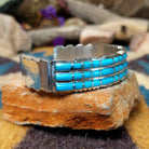 Handcrafted sterling silver three-row cuff by Sheldon Lalio featuring sleek channel inlay detailing across three parallel bands of turquoise with polished sterling silver craftsmanship; side view.