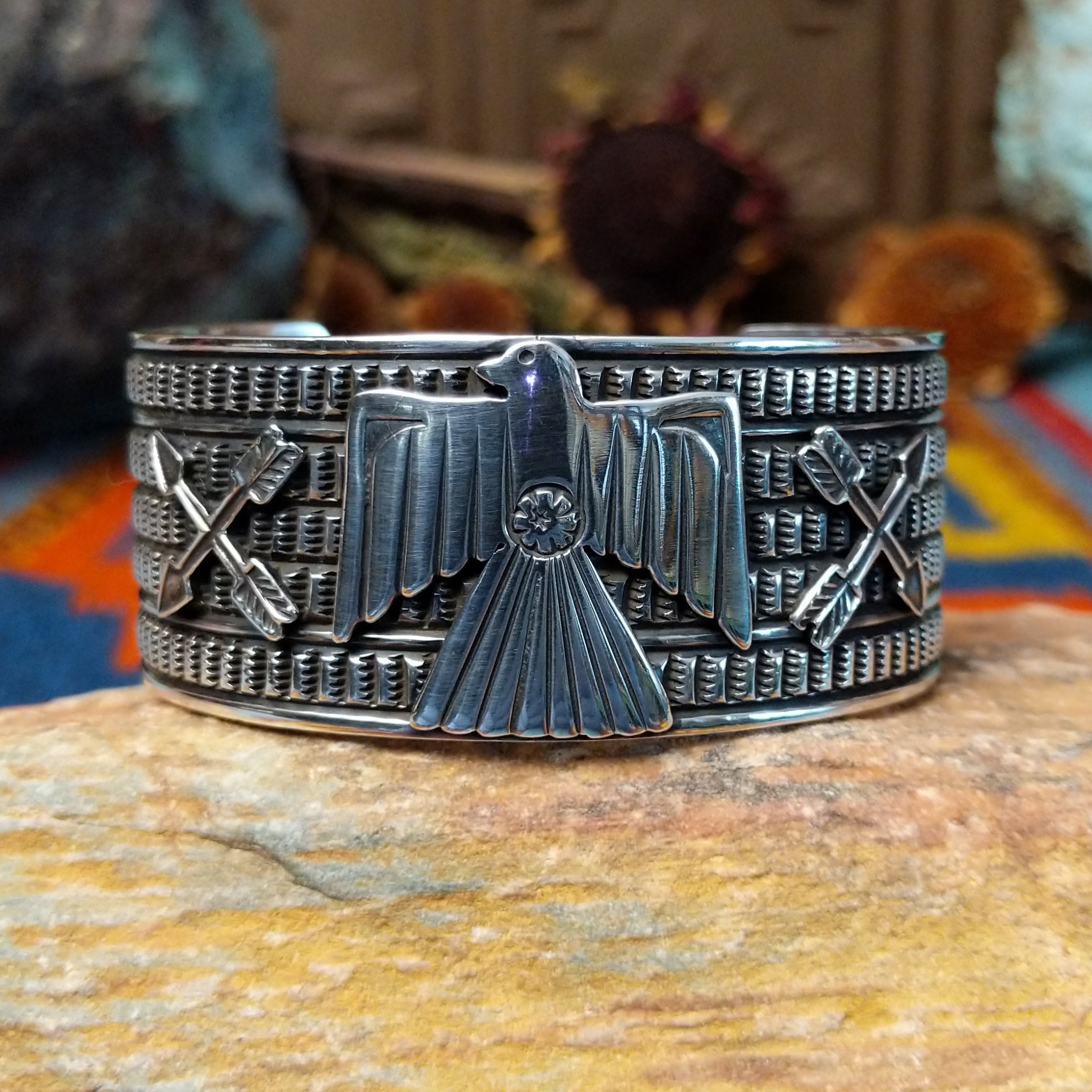 Wide silver cuff by J.O. White with raised thunderbird, crossed arrows, and stamped background.