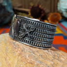 Wide silver cuff by J.O. White with raised thunderbird, crossed arrows, and stamped background.