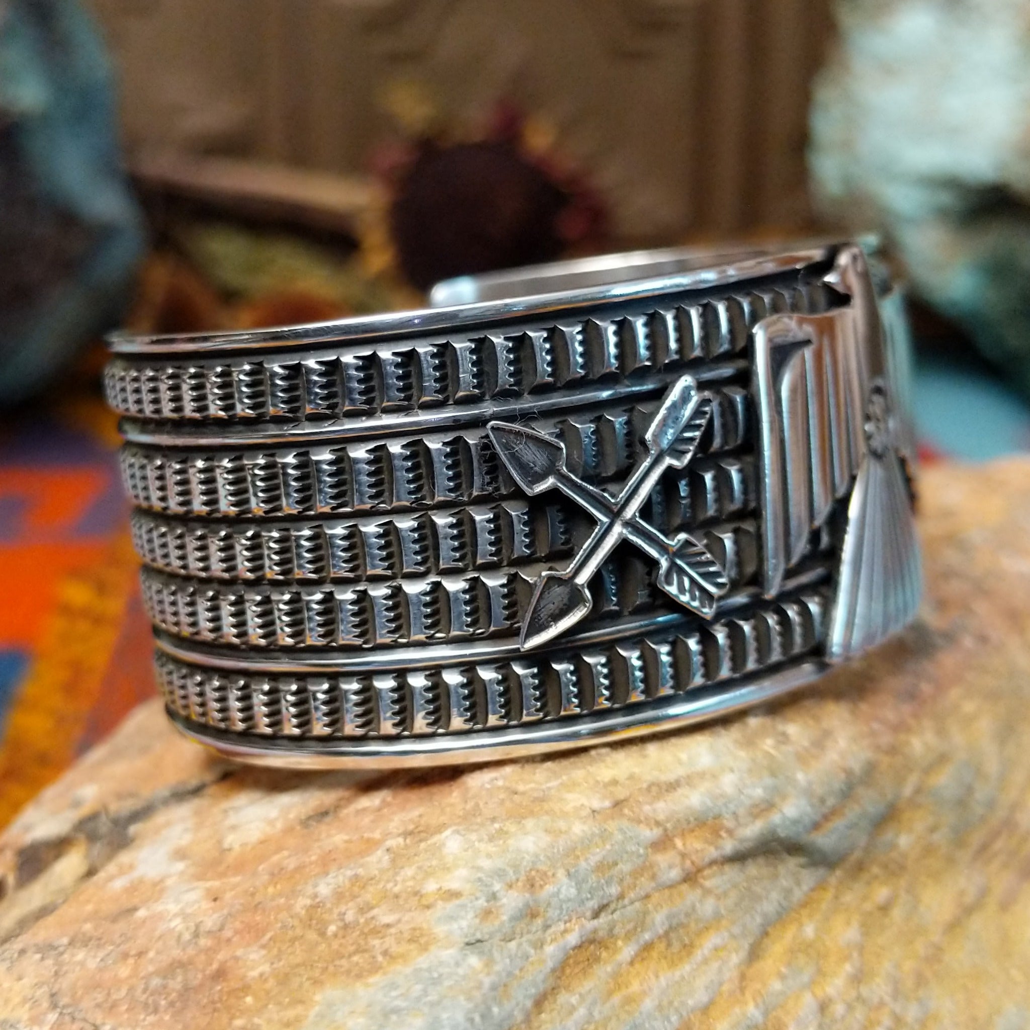 Wide silver cuff by J.O. White with raised thunderbird, crossed arrows, and stamped background.