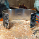 Wide silver cuff by J.O. White with raised thunderbird, crossed arrows, and stamped background.