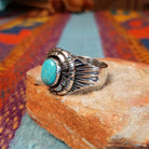 Tiered Turquoise Ring by Augustine Largo featuring an oval blue turquoise cabochon in a serrated bezel, surrounded by layered, symmetrical silverwork with radiating stamped details; side view.
