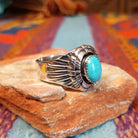 Tiered Turquoise Ring by Augustine Largo featuring an oval blue turquoise cabochon in a serrated bezel, surrounded by layered, symmetrical silverwork with radiating stamped details; side view.