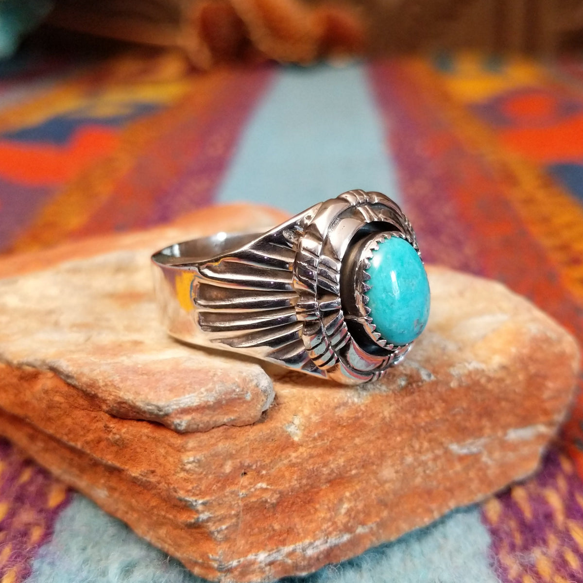 Tiered Turquoise Ring by Augustine Largo featuring an oval blue turquoise cabochon in a serrated bezel, surrounded by layered, symmetrical silverwork with radiating stamped details; side view.