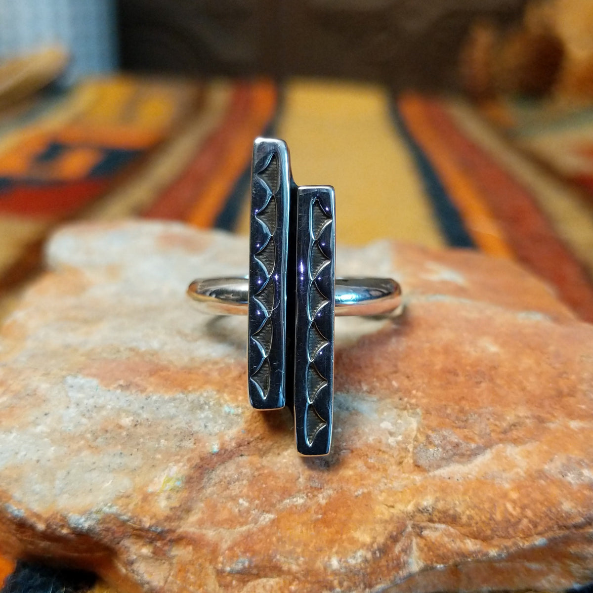 Front view of a silver ring by Diane Wylie showing two parallel bars of unequal height decorated with repeating triangular impressions and darkened detailing.