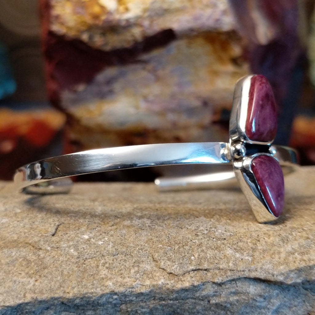 A sterling silver cuff displays two triangular purple spiny oyster shells and thin band.