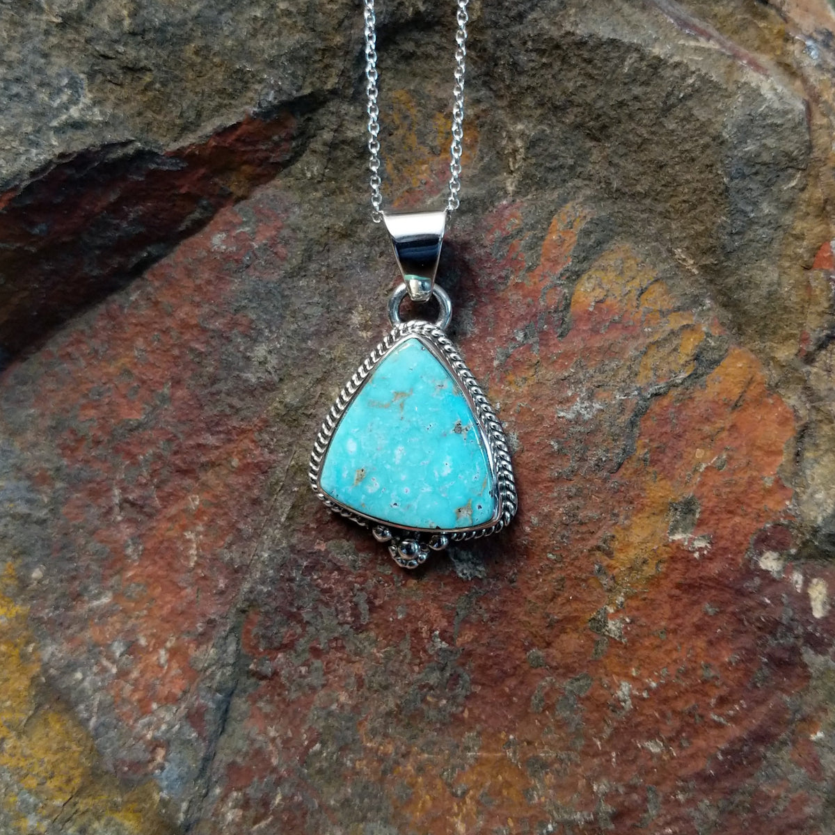 Triangular turquoise pendant by Burt Francisco featuring a bright blue turquoise stone framed with twisted sterling silver rope and decorative silver drops.