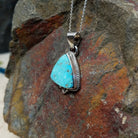 Triangular turquoise pendant by Burt Francisco featuring a bright blue turquoise stone framed with twisted sterling silver rope and decorative silver drops; side view.