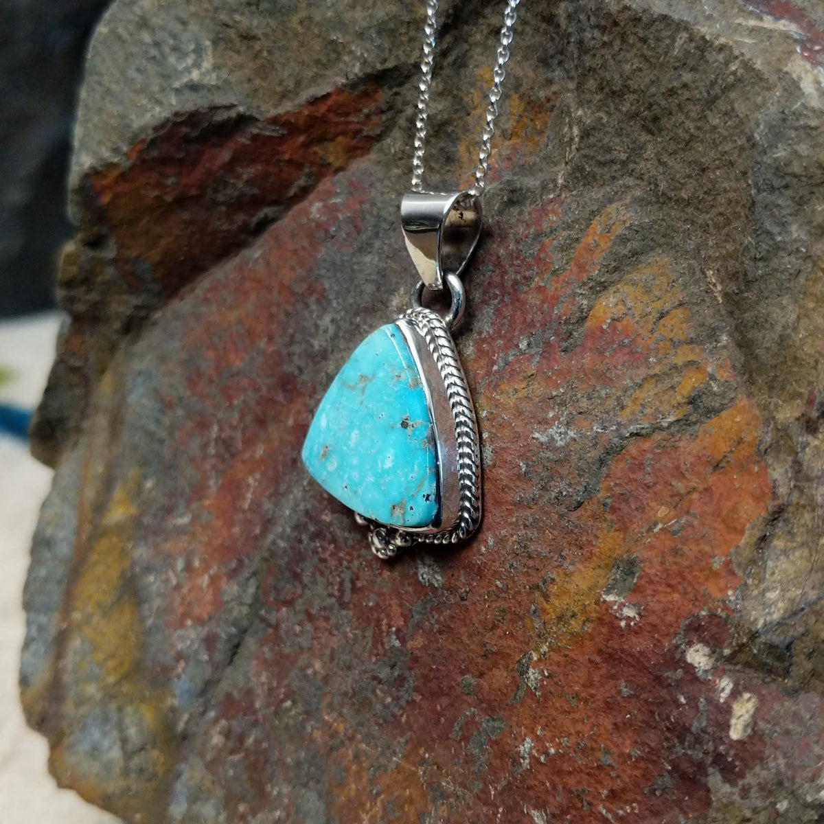 Triangular turquoise pendant by Burt Francisco featuring a bright blue turquoise stone framed with twisted sterling silver rope and decorative silver drops; side view.