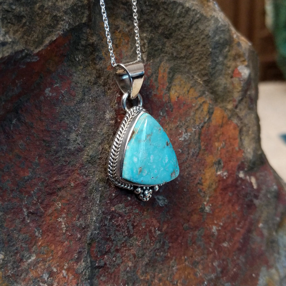 Triangular turquoise pendant by Burt Francisco featuring a bright blue turquoise stone framed with twisted sterling silver rope and decorative silver drops; side view.
