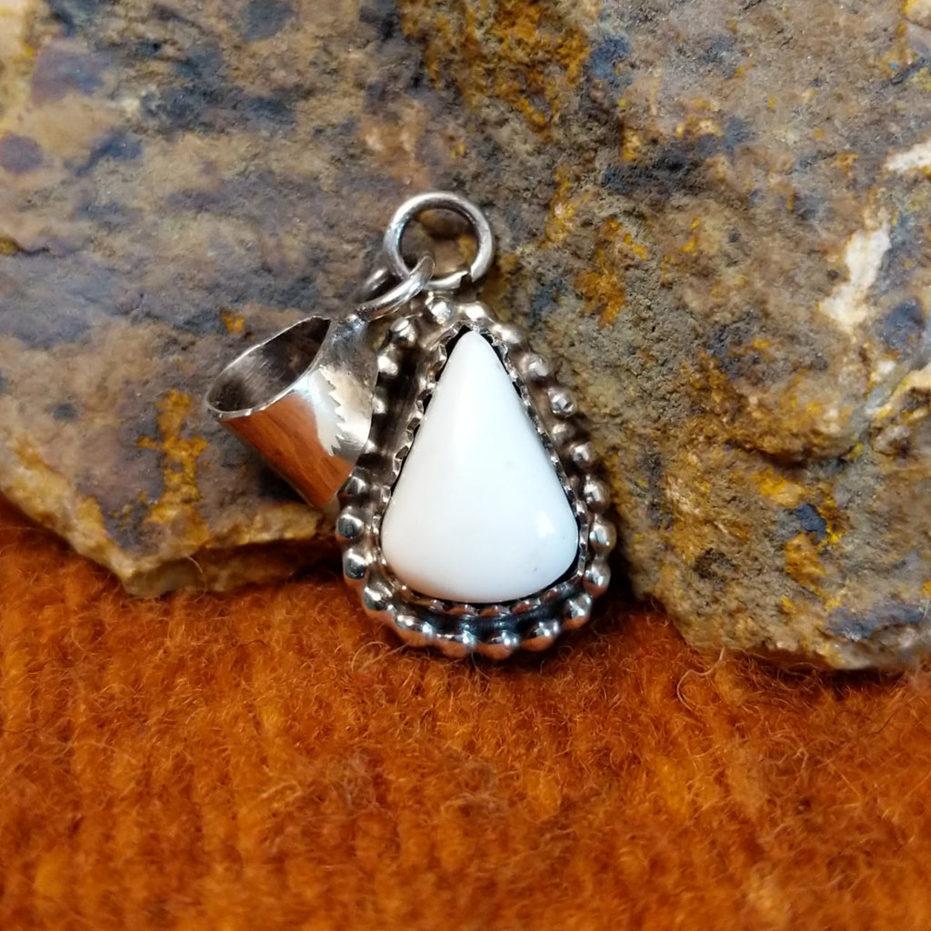 White buffalo set in a notched sterling silver bezel with intricately dotted frame.