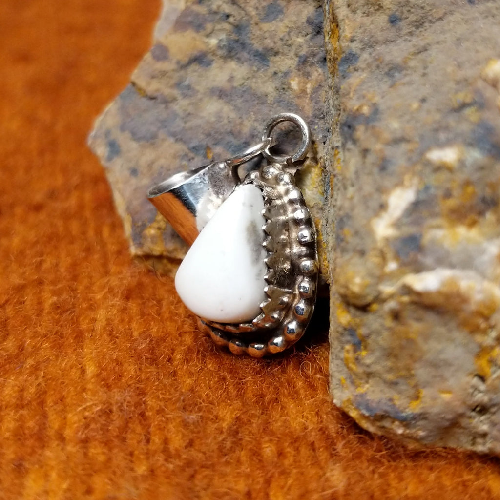 White buffalo set in a notched sterling silver bezel with intricately dotted frame.