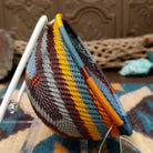 Handwoven triangular wire art bowl by Bridge for Africa featuring a spiral pattern in recycled wire with slate blue, mustard yellow, charcoal, brown, and gray tones, ideal for home décor or wall display; side view.