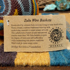 Handwoven triangular wire art bowl by Bridge for Africa featuring a spiral pattern in recycled wire with slate blue, mustard yellow, charcoal, brown, and gray tones, ideal for home décor or wall display; artisan information.