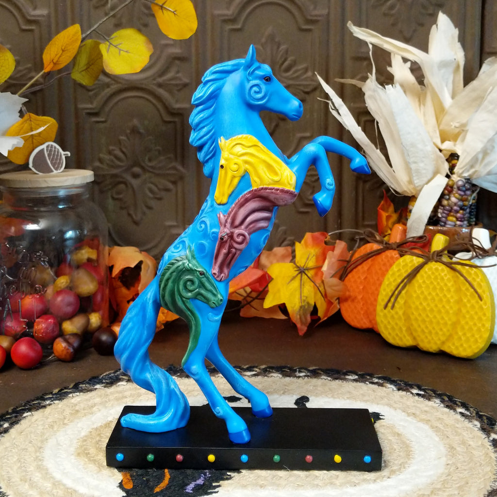 Pony in a rearing position painted blue with yellow, purple, and green horse heads on the body.