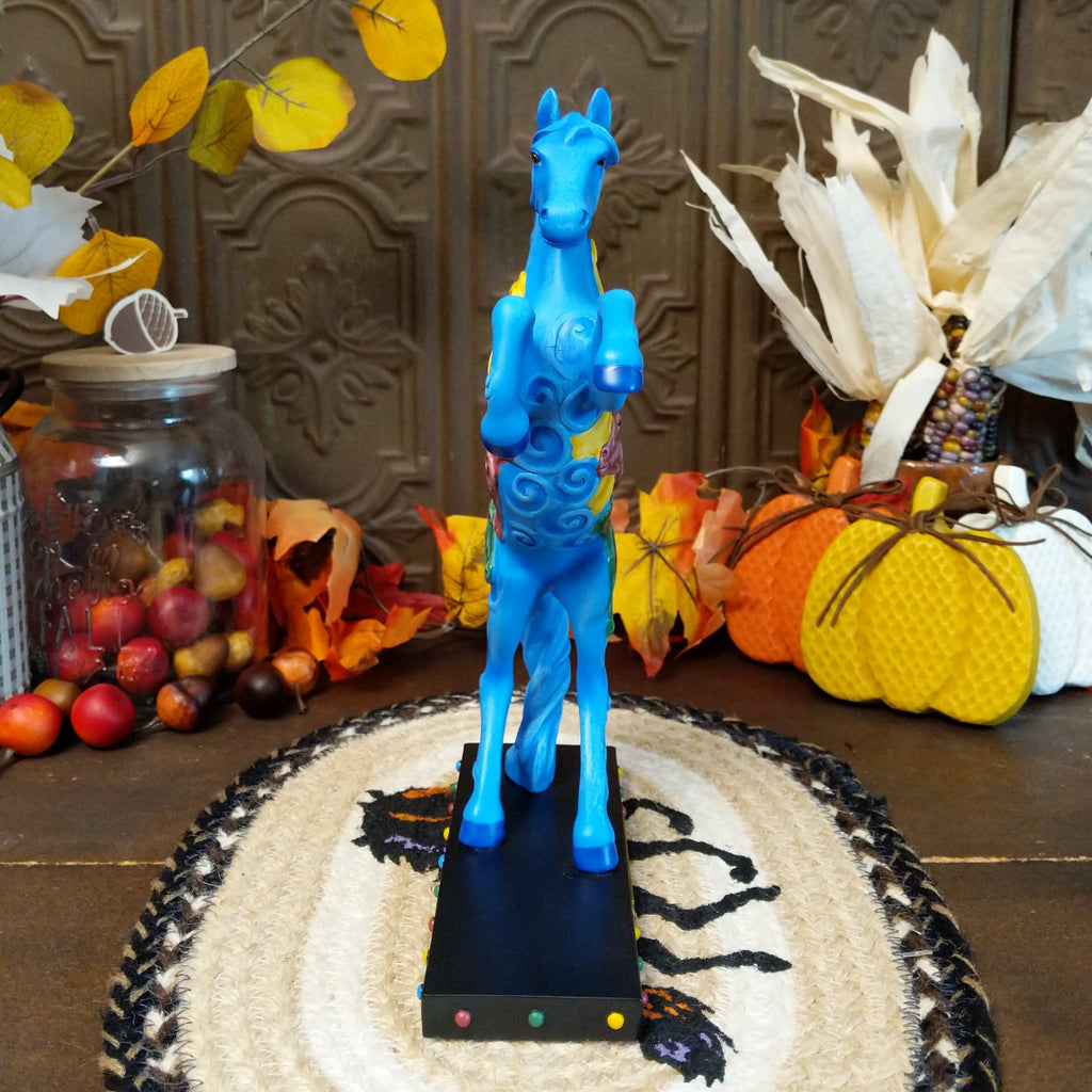 Pony in a rearing position painted blue with yellow, purple, and green horse heads on the body.