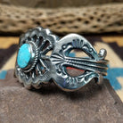 Turquoise cuff by Eugene Mitchell, featuring an oval blue turquoise stone set in a handcrafted sterling silver cuff with an intricate floral cutout design; side view.