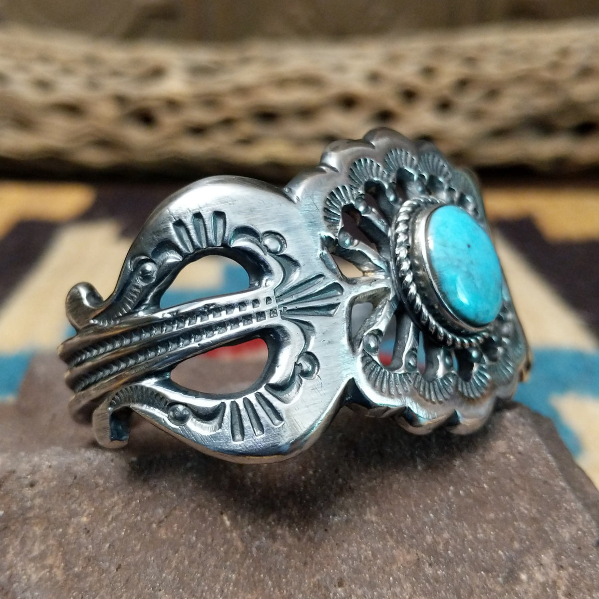 Turquoise cuff by Eugene Mitchell, featuring an oval blue turquoise stone set in a handcrafted sterling silver cuff with an intricate floral cutout design; side view.