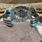 Turquoise cuff by Eugene Mitchell, featuring an oval blue turquoise stone set in a handcrafted sterling silver cuff with an intricate floral cutout design; underside view.