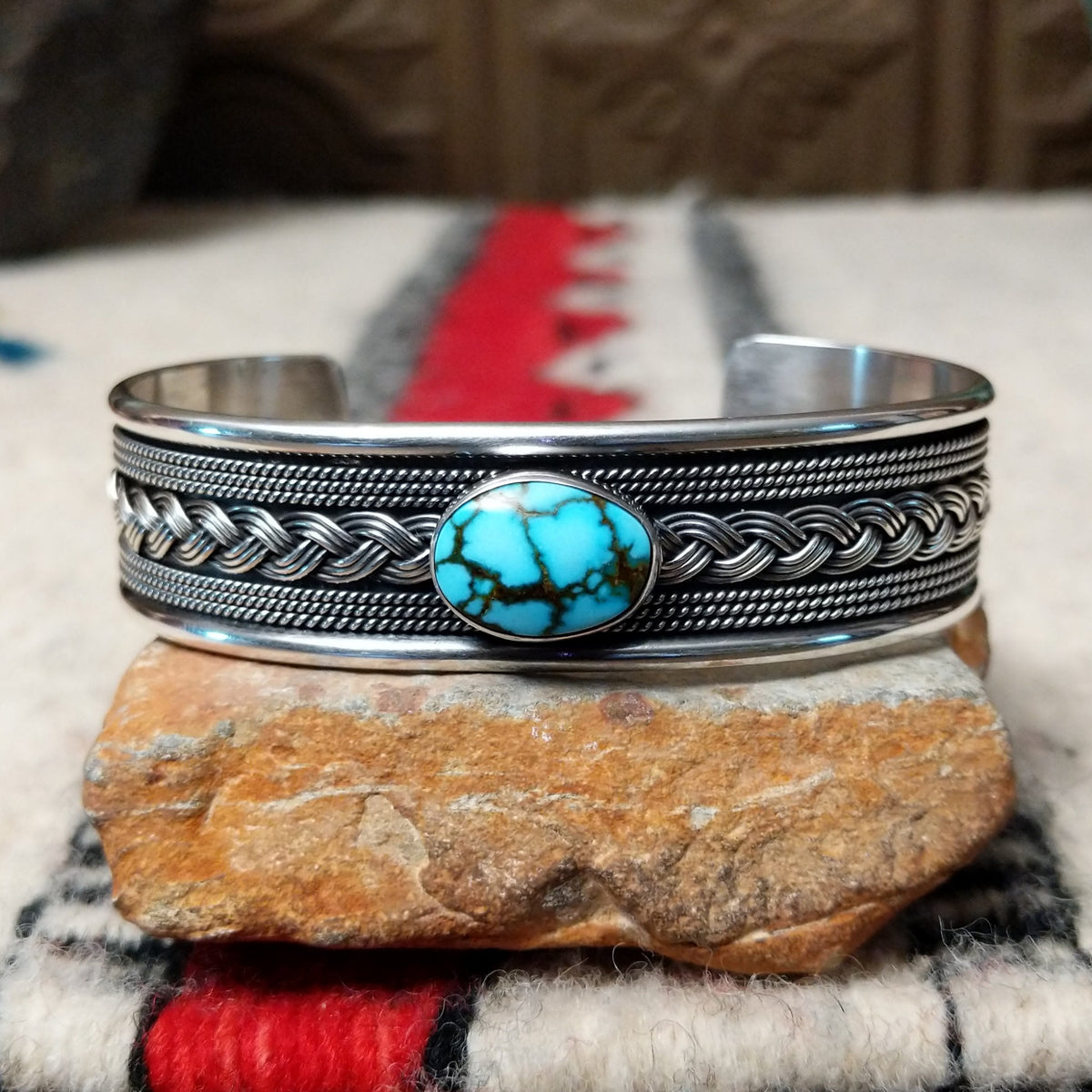 Silver cuff by H.M. featuring an oval blue turquoise stone with brown matrix, centered over an intricate braided silver band with twisted-wire detailing and oxidized accents.