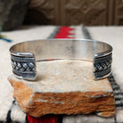 Silver cuff by H.M. featuring an oval blue turquoise stone with brown matrix, centered over an intricate braided silver band with twisted-wire detailing and oxidized accents; underside view.