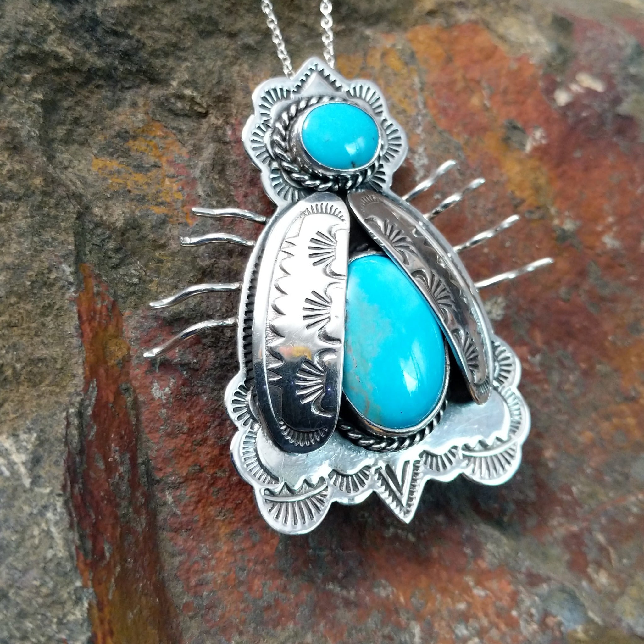 Handcrafted sterling silver bug pin with two turquoise stones and hand-stamped Navajo details; side view.