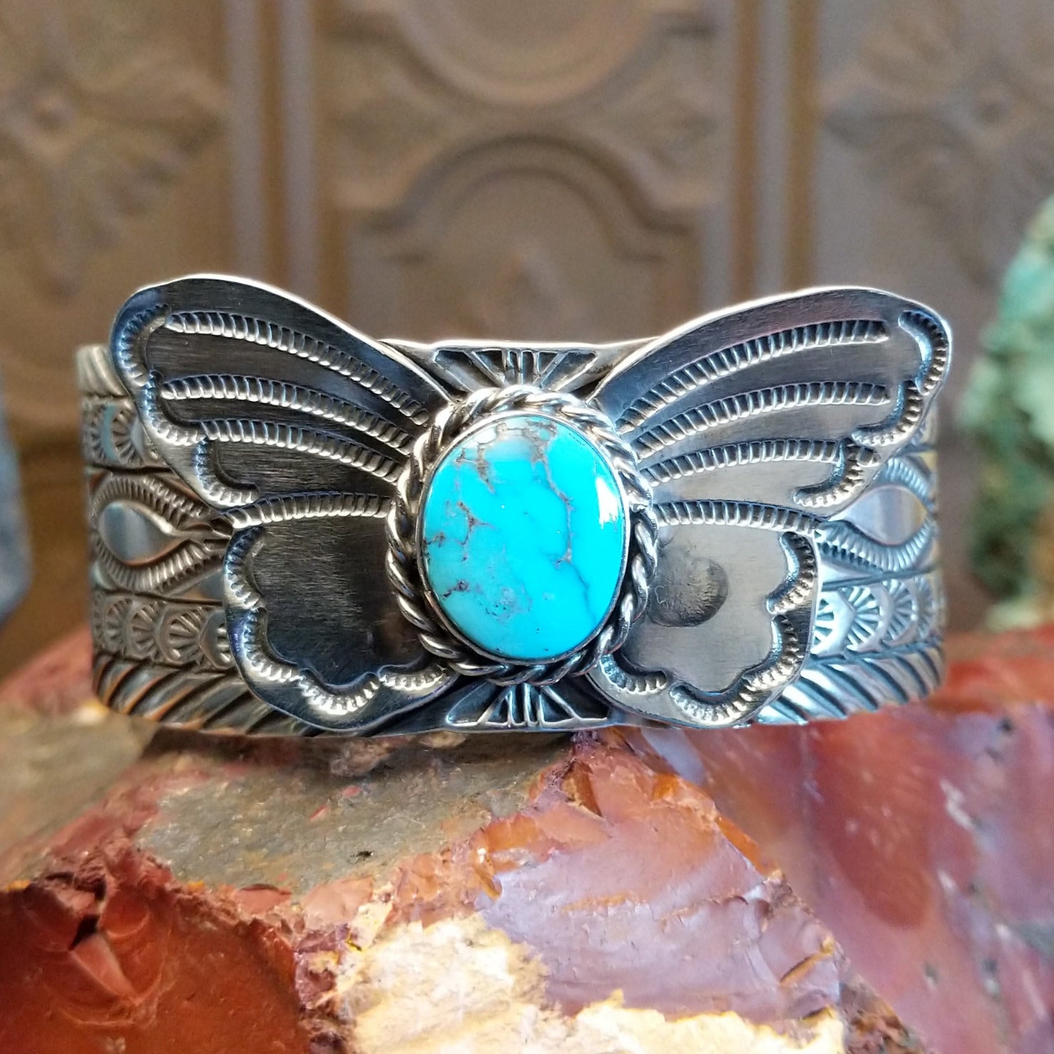 Sterling silver cuff bracelet with butterfly motif, turquoise set in round bezel that is framed by twisted rope detailing, and stamped designs along the surface of the piece.