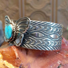 Sterling silver cuff bracelet with butterfly motif, turquoise set in round bezel that is framed by twisted rope detailing, and stamped designs along the surface of the piece.