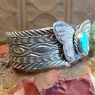 Sterling silver cuff bracelet with butterfly motif, turquoise set in round bezel that is framed by twisted rope detailing, and stamped designs along the surface of the piece.