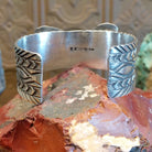 Sterling silver cuff bracelet with butterfly motif, turquoise set in round bezel that is framed by twisted rope detailing, and stamped designs along the surface of the piece.