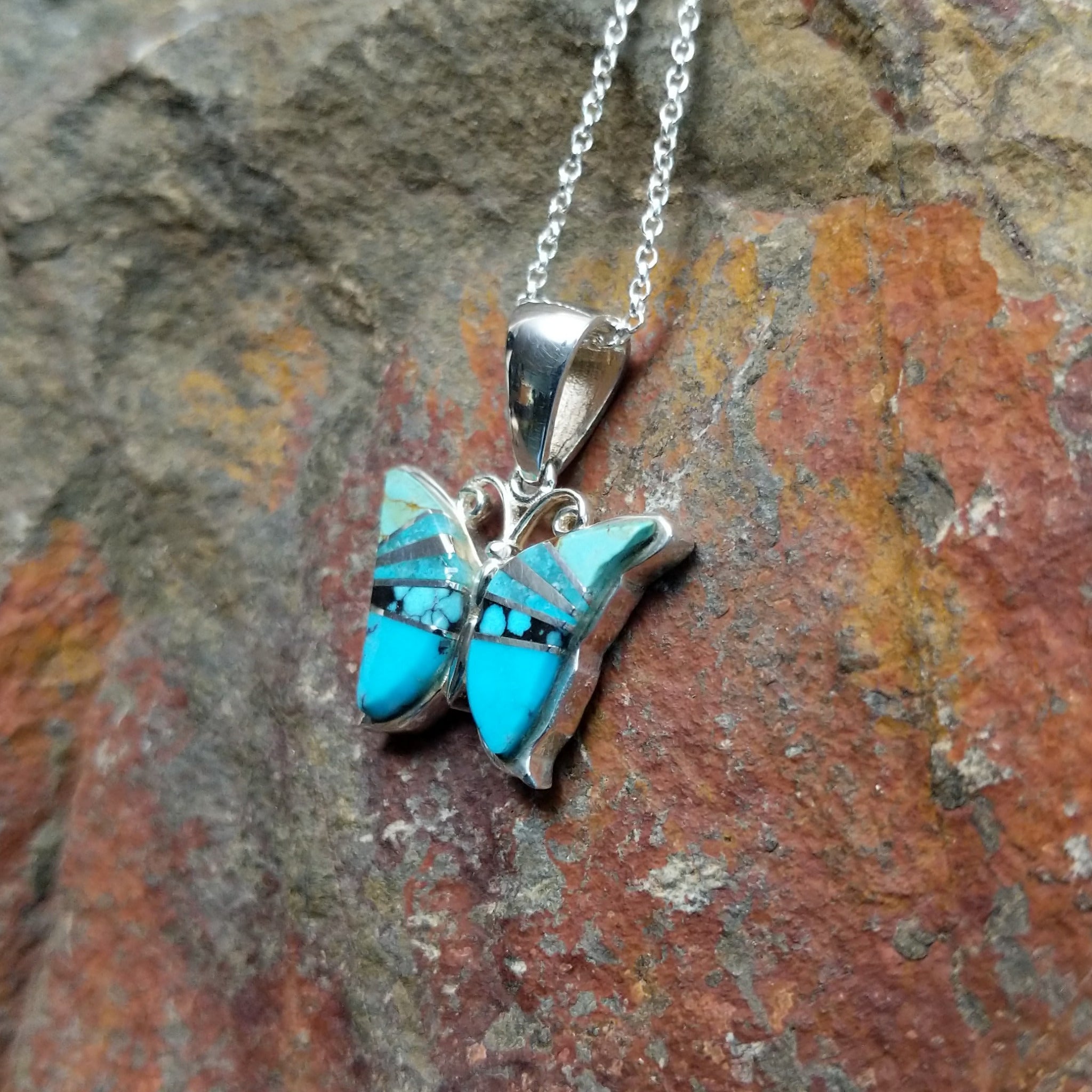 Handcrafted sterling silver turquoise butterfly pendant by Valerie Yazzie, featuring different shades of turquoise inlay in a butterfly design; side view.