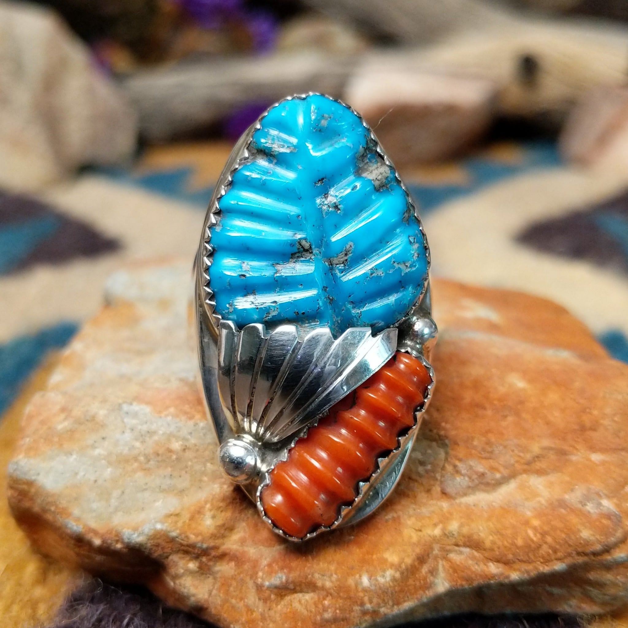 Sterling silver turquoise and coral ring by Lyolita Tsatte featuring a carved blue turquoise stone and ribbed red coral accent.