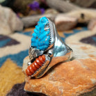 Sterling silver turquoise and coral ring by Lyolita Tsatte featuring a carved blue turquoise stone and ribbed red coral accent; side view.