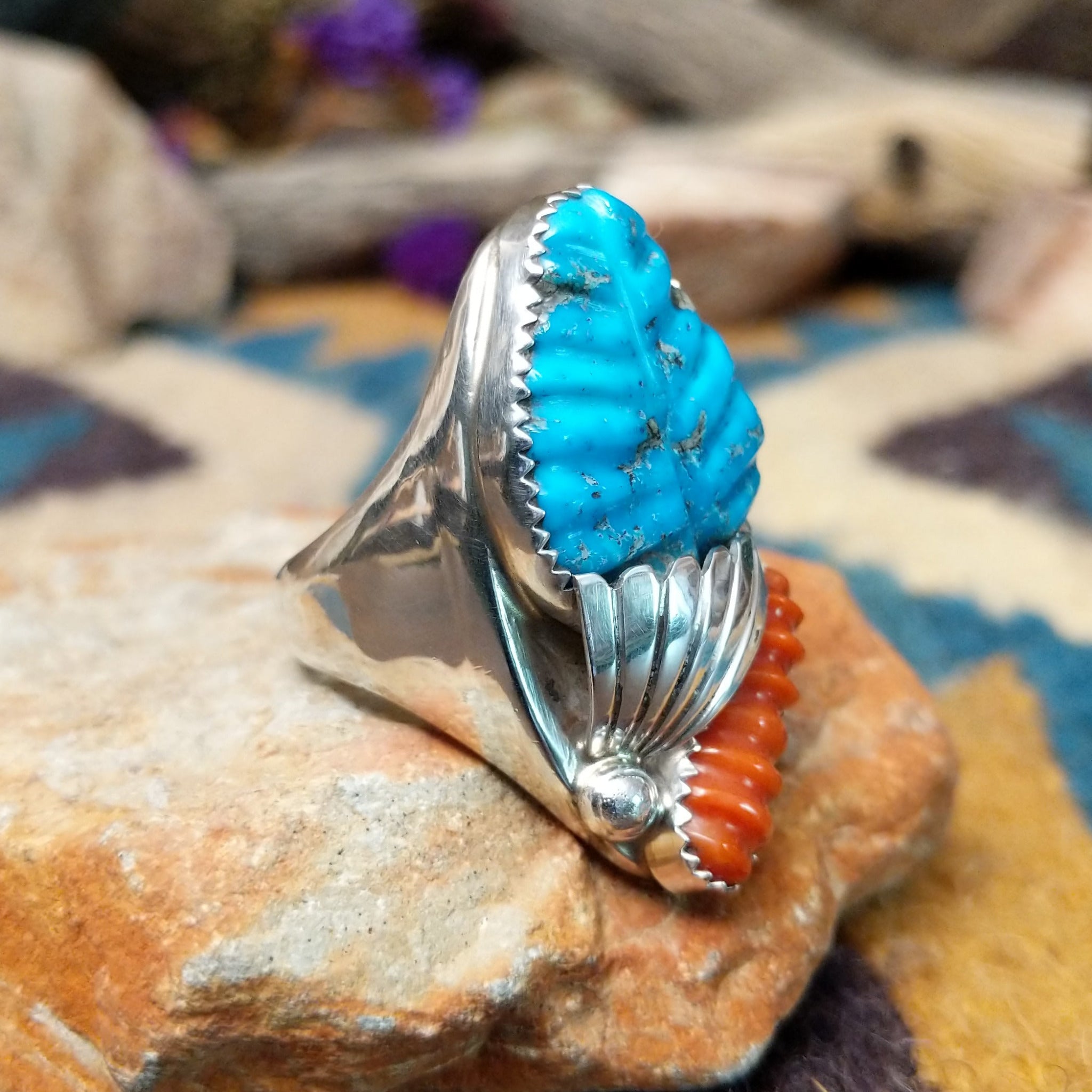 Sterling silver turquoise and coral ring by Lyolita Tsatte featuring a carved blue turquoise stone and ribbed red coral accent; side view.